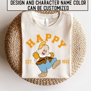 Könnte beinhalten: Ein weißes T-Shirt mit einem Cartoon-Bild eines Zwergs in einem blauen und braunen Outfit. Der Text "HAPPY" ist in Gelb über dem Zwerg und "EST. 1953" ist unter dem Zwerg.
