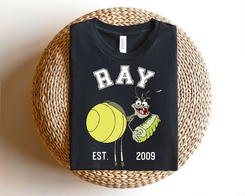 Puede incluir: Camiseta negra con una imagen de dibujos animados de Ray de La Princesa y el Sapo de Disney. El texto "RAY" est&aacute; en blanco con un contorno blanco. El texto "EST. 2009" tambi&eacute;n est&aacute; en blanco.