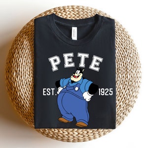 Puede incluir: Camiseta negra con una imagen de dibujos animados de Pete el cachorro con un mono y el texto "PETE EST. 1925".