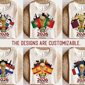 May include: Cream-coloured t-shirts displaying FIFA World Cup 2026 designs. Each shirt showcases a gold trophy, flags, and cityscapes representing Panama, Portugal, Qatar, Paraguay, Spain, and France. The text "2026 FIFA World Cup" is visible on each shirt.