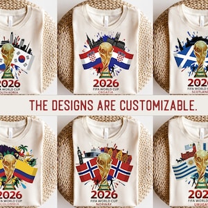 May include: A collection of cream-coloured t-shirts, each showcasing a FIFA World Cup 2026 design. The shirts display a golden trophy, flags, and cityscapes representing South Korea, Croatia, Scotland, Colombia, Norway, and Uruguay. Text reads "2026 FIFA World Cup". The text "THE DESIGNS ARE CUSTOMIZABLE" is also present.