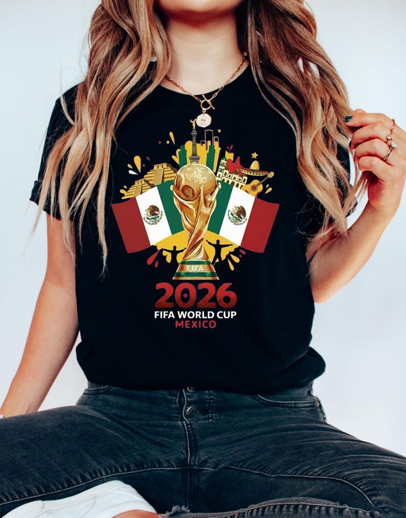 May include: Black t-shirt with a gold FIFA World Cup trophy, Mexican flags, and the text "2026 FIFA WORLD CUP MEXICO". The design incorporates Mexican cultural symbols and a cityscape.