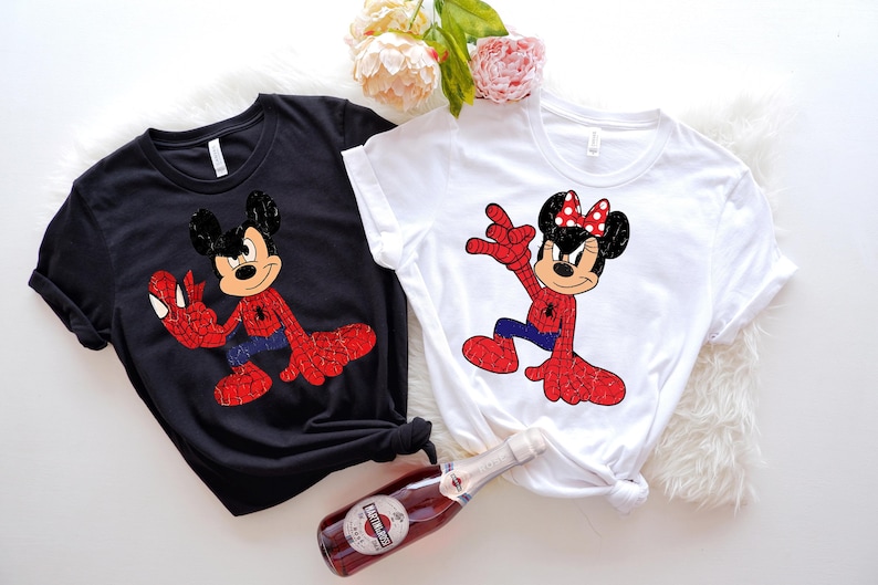 May include: Two t-shirts, one black and one white, each featuring a cartoon character in a Spider-Man costume. The black shirt has Mickey Mouse, and the white shirt has Minnie Mouse. Both characters are in a dynamic pose with red and blue accents.