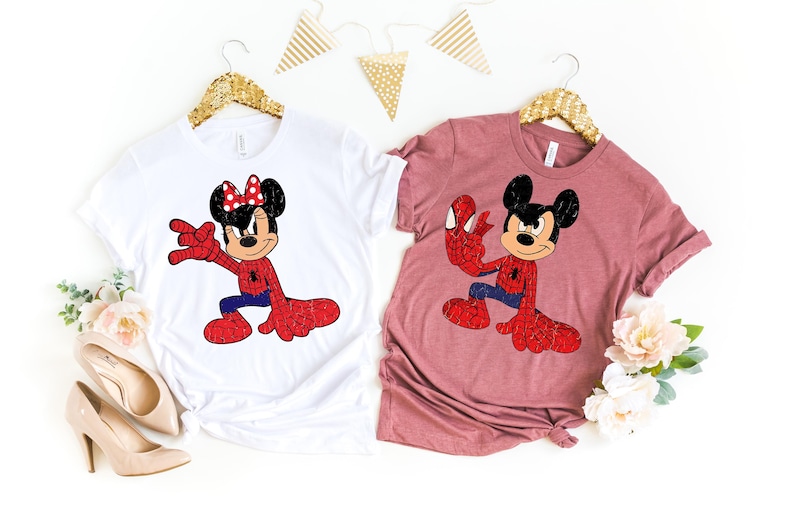 May include: Two t-shirts, one white and one mauve, each featuring a cartoon character dressed as Spider-Man. The white shirt has Minnie Mouse, and the mauve shirt has Mickey Mouse. Both characters are in a Spider-Man pose, with red and blue outfits.