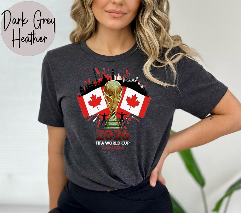 May include: Dark grey heather t-shirt with a graphic celebrating the 2026 FIFA World Cup in Canada. The design includes the World Cup trophy, Canadian flags, and the text "2026 FIFA WORLD CUP CANADA".
