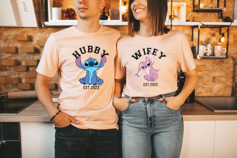 May include: Two peach-coloured t-shirts featuring a cartoon Stitch character. The shirt on the left says "Hubby Est. 2022" and the shirt on the right says "Wifey Est. 2022".
