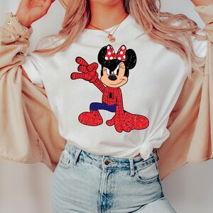 May include: White t-shirt with a cartoon mashup of Minnie Mouse as Spider-Man. The design shows a red and blue Spider-Man suit with a Minnie Mouse head, including a red bow with white polka dots. The shirt is worn by a person.