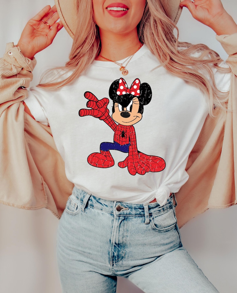 May include: White t-shirt with a cartoon mashup of Minnie Mouse as Spider-Man. The design shows a red and blue Spider-Man suit with a Minnie Mouse head, including a red bow with white polka dots. The shirt is worn by a person.