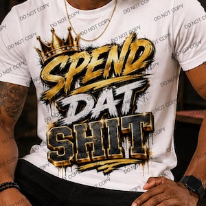 May include: A white short-sleeved t-shirt featuring a graphic design with a gold crown icon above the text SPEND DAT SHIT in a bold, metallic-style font with black and gold coloring. The design includes paint splatter effects and a graffiti aesthetic.