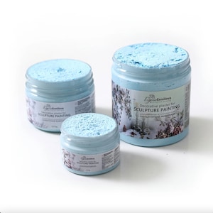 Op de afbeelding: Drie potten met lichtblauwe decoratieve pleister voor beeldhouwkunst. De potten zijn gelabeld met "Decoratieve pleister voor BEELDHOUWKUNST" en "СКУЛЬПТУРНОЙ живопис".