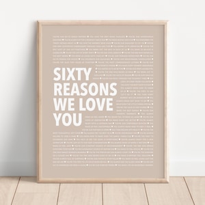 May include: A framed print with a beige background and white text that reads "Sixty Reasons We Love You".