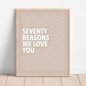 May include: A framed print with a beige background and white text that reads "Seventy Reasons We Love You".