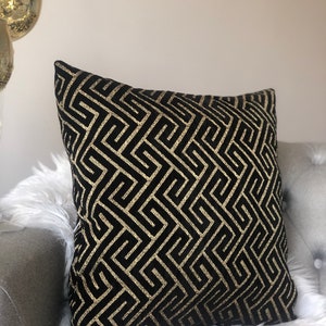 May include: Black and gold geometric patterned throw pillow. The pillow has a black background with a gold geometric pattern.