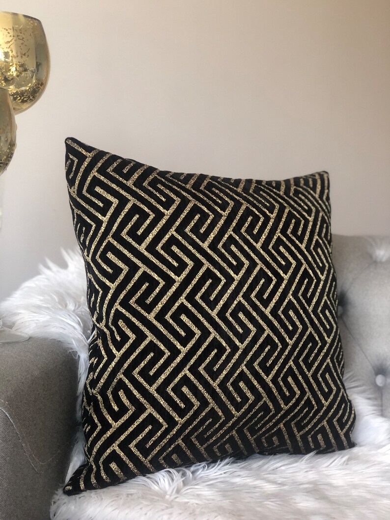 May include: Black and gold geometric patterned throw pillow. The pillow has a black background with a gold geometric pattern.