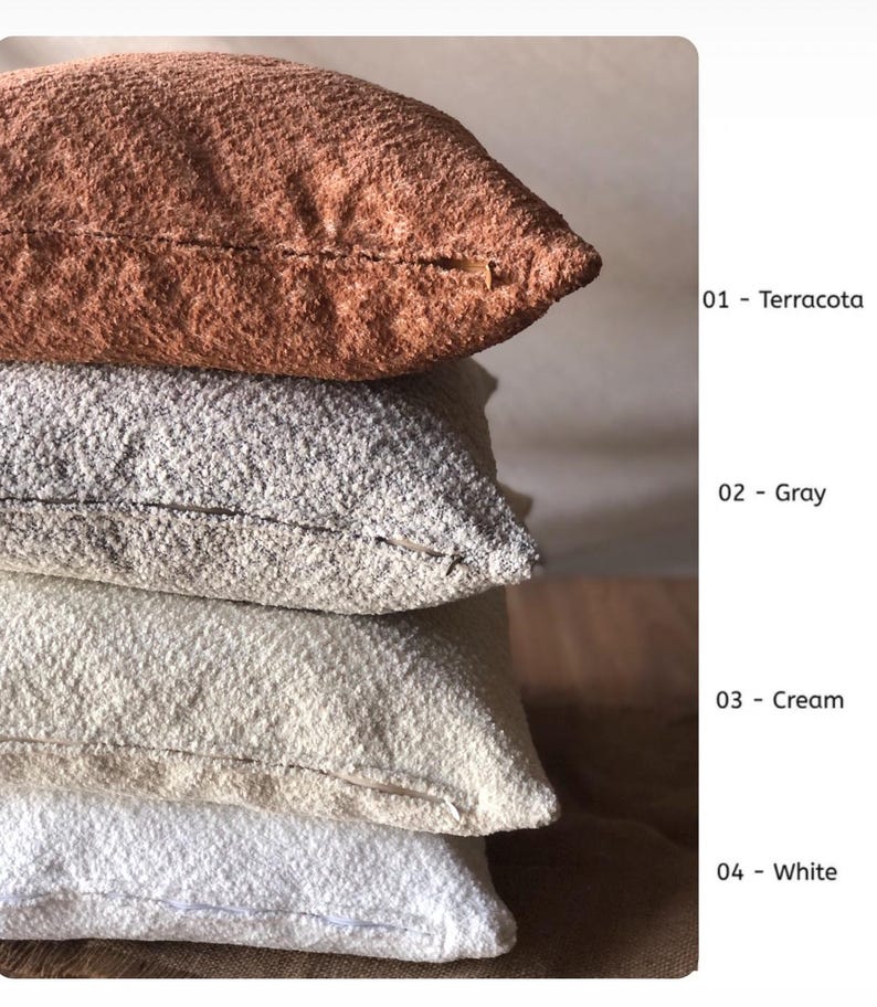 May include: A stack of four square throw pillows with a textured, nubby fabric surface. The colors from top to bottom are labeled as 01 - Terracota, 02 - Gray, 03 - Cream, and 04 - White. Each pillow features a visible side seam and zipper closure.