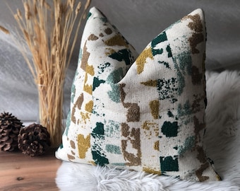 May include: A white throw pillow with a geometric pattern in shades of green, brown, and yellow. The pillow is made of a textured fabric and has a square shape.