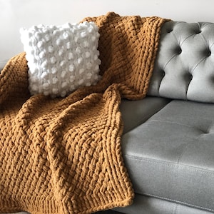 May include: A mustard yellow chunky knit throw blanket draped over a gray tufted sofa with a white textured throw pillow.