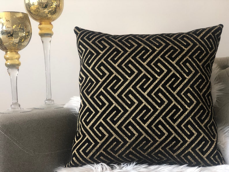 May include: Black and gold geometric patterned throw pillow. The pillow has a black background with a gold geometric pattern.