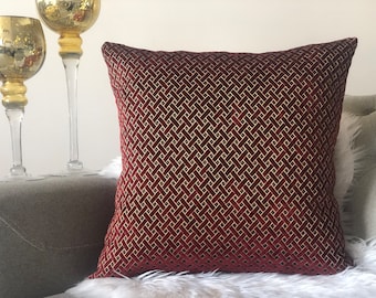 May include: A red velvet throw pillow with a gold geometric pattern. The pillow is on a couch with a white fur throw.