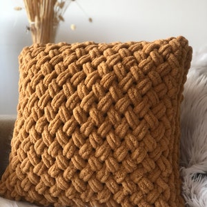 Könnte beinhalten: Ein gelbes, gestricktes Kissen mit einem gewebten Muster. Das Kissen ist aus einem weichen, plüschigen Stoff.