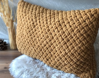 Könnte beinhalten: Ein braunes gestricktes Kissen mit einem gewebten Muster. Das Kissen liegt auf einer weißen Kunstfell-Oberfläche.
