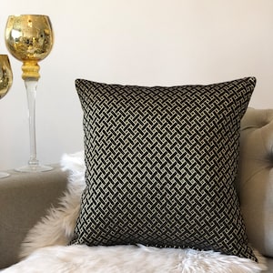 May include: Black and gold geometric patterned throw pillow. The pillow is on a white faux fur throw and a gray couch.