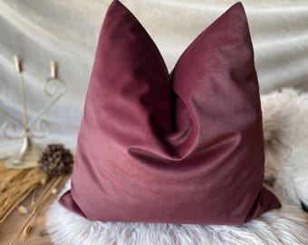 Può includere: Un cuscino in velluto bordeaux scuro con una texture morbida e soffice. Il cuscino è piegato a metà, creando una forma rotonda e liscia.