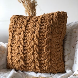 May include: A brown knitted throw pillow with a textured woven pattern. The pillow is sitting on a white faux fur blanket.