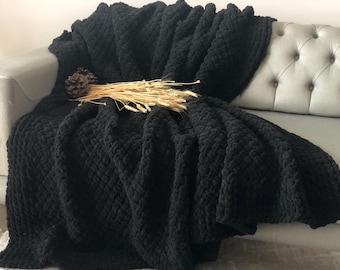May include: A black knitted throw blanket with a textured diamond pattern, draped over a gray couch.