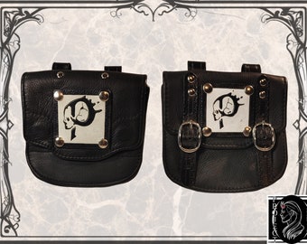 May include: Two black leather bags with silver buckles and studs. Each bag has a silver square patch with a black and white skull design.