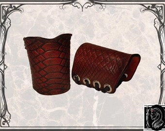 May include: A pair of brown leather wrist cuffs with a snakeskin pattern. The cuffs have a lace-up closure with metal eyelets.