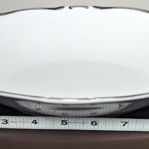 May include: A white oval serving bowl with a silver rim and a scalloped edge. The bowl is 18 cm wide.