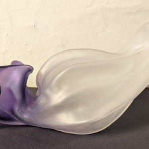 Puede incluir: Un jarrón de vidrio esmerilado con un efecto degradado morado. El jarrón tiene forma de flor con una abertura ancha y un cuello estrecho.