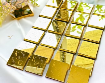 May include: A collection of square gold-toned acrylic favors arranged in a grid. Each piece features custom laser-engraved text including the initials K&G, the names Kaitlyn and Gabriel, and the date 04.04.25, alongside various floral motifs.