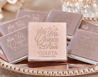 Könnte beinhalten: Eine Sammlung quadratischer, roségoldfarbener Schokoladenpräsente in Metallfolie. Jedes Stück zeigt ein aufgedrucktes Design mit einer Krone, Sternen sowie dem Text 'Mis Quince Años', 'VIOLETA' und dem Datum '27 diciembre 2024' in Schreibschrift.