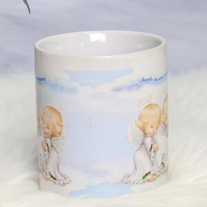May include: White ceramic mug with a blue and white sky background featuring two angels with halos and wings. The text "Angels are never too far away" is printed on the mug.