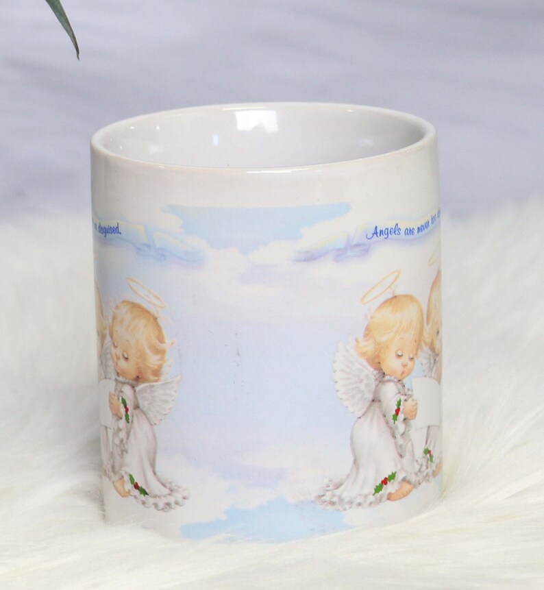 May include: White ceramic mug with a blue and white sky background featuring two angels with halos and wings. The text "Angels are never too far away" is printed on the mug.