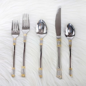 May include: A set of five silver-toned flatware pieces with gold accents. The set includes a knife, two forks, and two spoons.