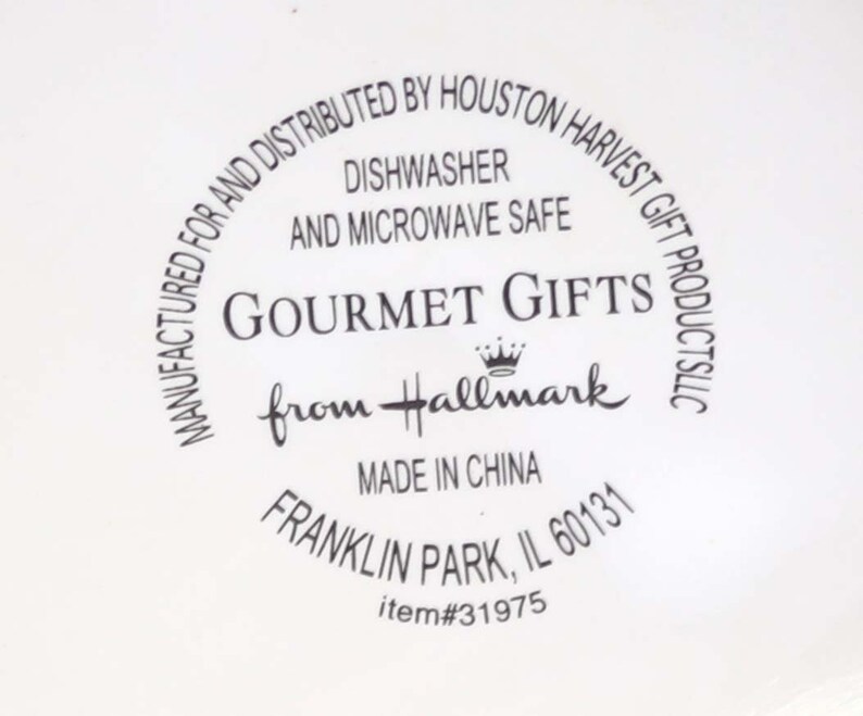May include: A white ceramic plate with black text that reads "Manufactured for and distributed by Houston Harvest Gift Products LLC. Dishwasher and microwave safe. Gourmet Gifts from Hallmark. Made in China. Franklin Park, IL 60131. Item #31975."