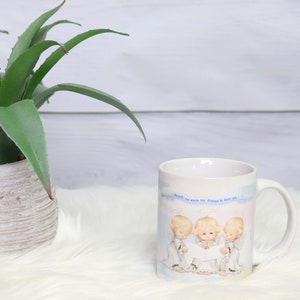 May include: White ceramic mug with a blue and white illustration of three angels singing. The text on the mug reads "Angels are never too distant to hear you."