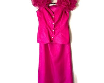 May include: A vibrant fuchsia two-piece formal dress. The top features a tailored bodice with pearl-like buttons and dramatic ruffled sleeves. The skirt is a long, straight style. The dress is hanging on a black hanger against a white background.