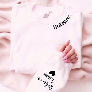 Könnte beinhalten: Ein rosa Sweatshirt mit dem Wort "mama" und einem Herz auf der Vorderseite und den Worten "Rebecca I love you" und einem Herz auf dem Ärmel.