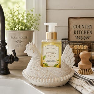 May include: A cream-colored ceramic chicken-shaped soap holder containing a clear bottle of Bath & Body Works Kitchen Lemon gentle and clean foaming hand soap with a gold pump dispenser and a label featuring lemon illustrations.