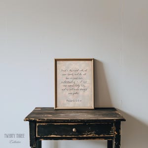 Puede incluir: Una impresión enmarcada con el texto "Confía en el Señor con todo tu corazón, y no te apoyes en tu propia comprensión." La impresión está en un marco dorado y descansa sobre una mesa de madera negra.