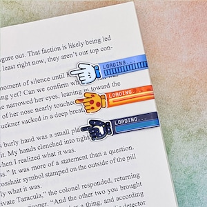 May include: Three colorful bookmarks with a hand pointing to the right and a progress bar that says "LOADING..."  The bookmarks have a blue, orange, and dark blue background. The hand on the blue bookmark is light blue, the hand on the orange bookmark is orange with a pizza slice, and the hand on the dark blue bookmark is dark blue with a crescent moon and stars.