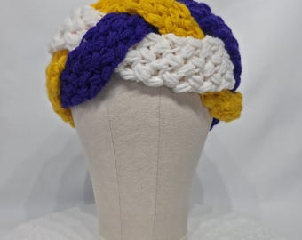 May include: A handmade crochet hat in a woven pattern, displayed on a mannequin head. The hat features alternating bands of white, gold, and purple yarn. The hat is a unique, colorful accessory.