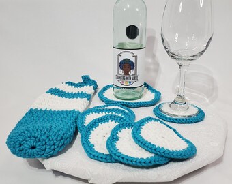 May include: Set of crocheted teal and white coasters with a teal crocheted bottle cozy. The coasters are round and have a white center with a teal border. The bottle cozy is striped and has a white label with the text "Crocheting with Auntie".