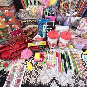 May include: A collection of colorful stationery, kitchenware, and accessories, including notebooks, pens, pencils, and red kitchen utensils. Themed items include watermelon and fruit designs, with a recipe book and air fryer cookbook.