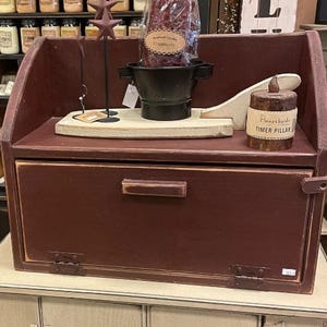 May include: A red wooden bread box with a white top and a single door. The bread box has a small shelf above the door and a decorative star on the top.