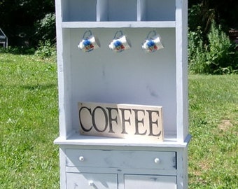 May include: White painted wooden cabinet with three drawers and a door. The cabinet has a hutch with three shelves and a sign that says "COFFEE".